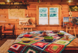 Warme houten lodge met een kleurrijk gehaakt tafelkleed, keramieken kommen en schilderijen in de ruimte.