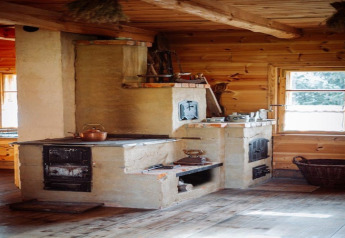 Oude houtkachel in een gezellige houten lodge, met zonlicht dat door het raam de warme sfeer versterkt.