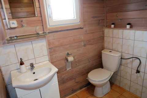 Badezimmer in einer Holzhütte mit Waschbecken, Toilette, Fenster und kleinen Kaktuspflanzen.