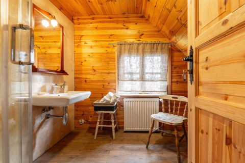 Wood-paneled bathroom at House by the road Skansen, Bełczna, featuring a sink, mirror, chair, and window.