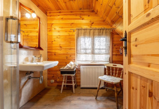 Rustikales Badezimmer aus Holz in House by the road Skansen, Bełczna, mit Waschbecken, Spiegel und Stuhl.