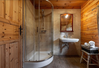 Wood-paneled lodge bathroom featuring a shower, wall-mounted sink, mirror, and basket of rolled towels.