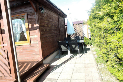 Buitenpatio bij een houten chalet met tafel, stoelen en parasol, omringd door groen onder de zon.