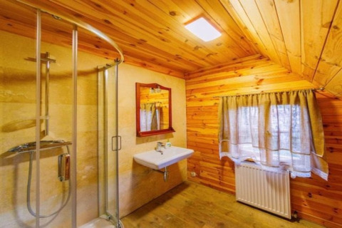 Badezimmer in einer Holzhütte mit moderner Dusche, Waschbecken, Spiegel und Fenster mit Vorhängen.