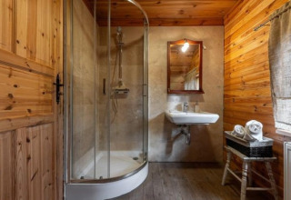 Photo of a rustic lodge bathroom featuring a glass shower, wall-mounted sink, wooden walls and a window.