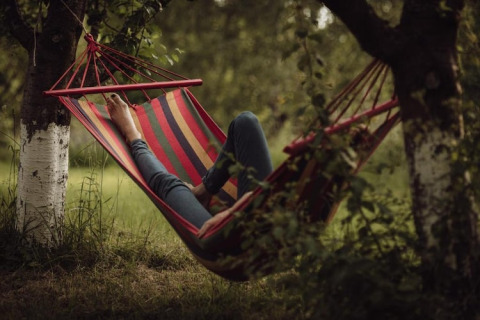 Een persoon rust in een kleurrijke hangmat tussen twee bomen bij House by the road Skansen in Bełczna.