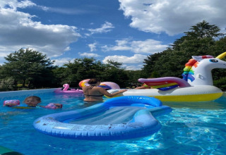 Mensen genieten van een zonnige dag in het lodgezwembad met kinderen en kleurrijke opblaas unicorns.