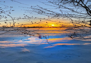Beautiful sunset over a snowy field viewed from a lodge, with tree branches framing the glowing sky.