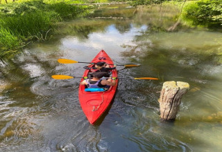 Two people kayaking in a red kayak on a narrow river near House by the road Skansen, Bełczna, Germany.