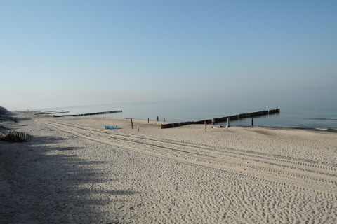 Ruhiger Strand mit klarer blauer Himmel und Holzbarrieren am Ufer, aufgenommen an einer Hütte in Deutschland.