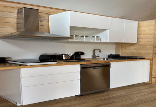 Moderne Küche im Haus am See Klępnica mit weißen Schränken, Holzverkleidung und Edelstahlgeräten.