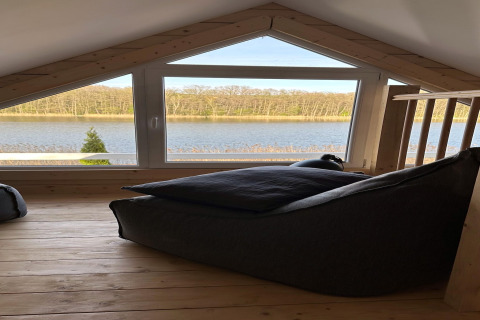 Loft area with large window overlooking Lake Klępnica in Germany, cozy beanbag and wooden floor.