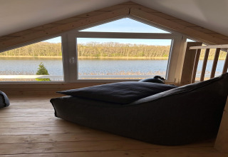 Ático con amplia ventana y vistas al lago Klępnica en Alemania, suelo de madera y sillón puff.