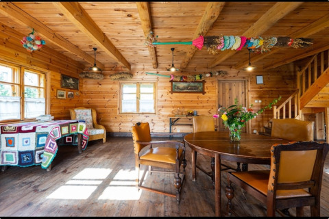 Rustic lodge interior with wooden walls, colorful decorations, round table and leather chairs in Bełczna.