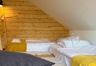 Et hyggeligt soveværelse med trævæg, to senge med gule tæpper og skrå loft, House by Lake Klępnica.
