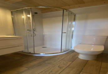 Bagno moderno con cabina doccia in vetro, WC e pavimento effetto legno alla House by Lake Klępnica in Germania.