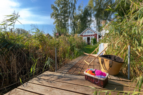 Houten steiger aan het meer met strandhuis, stoel en mand, omgeven door riet in Duitsland.