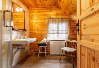 Badkamer met houten muren, wastafel, stoel en raam in een gezellige lodge in Bełczna, Duitsland