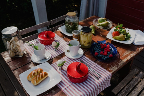 Outdoor breakfast at House by Lake Klępnica, Germany, with fruit, preserves, pastries, and tea on a rustic table.