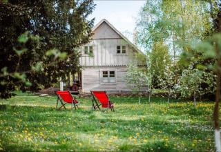 Two red chairs sit on a blooming lawn in front of the cottage 'House by the road Skansen' in Bełczna, Germany.
