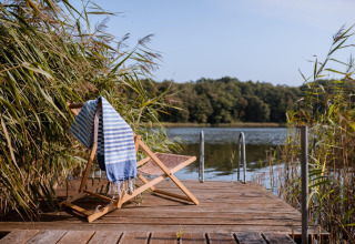 Silla de madera con toalla a rayas en un muelle junto al lago Klępnica, en una casa de playa en Alemania.