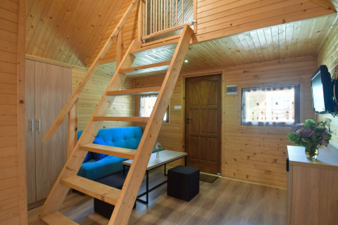 Interieur van een knusse houten chalet met blauwe sofa, trap naar de mezzanine en houten wanden.