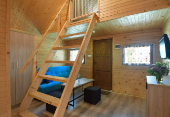 Innenaufnahme einer gemütlichen Holzhütte mit blauer Couch, Leiter zur Galerie und Holzwänden.