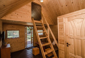Innenaufnahme einer Holzhütte mit Dachboden, Leiter und großen Fenstern in Holiday cottages Łazy, Dänemark.