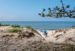 People walk through sand dunes towards the beach at Holiday cottages Łazy, with the sea in the background.