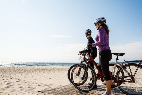Dos personas con bicicletas y cascos disfrutan de la vista al mar durante su estancia en un glamping en la playa.