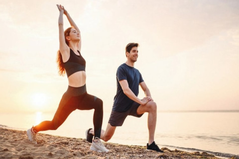 Two people stretching on a beach at sunset, exercising together near a glamping accommodation site.