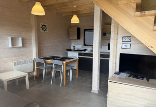Moderne opholdsstue og køkken i et to-etagers feriehus i Mielenko, med spisebord og tv under trappen.