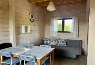 Hyggelig stue i to-etagers feriehus i Mielenko, Danmark, med spisebord og sofa ved vinduet.