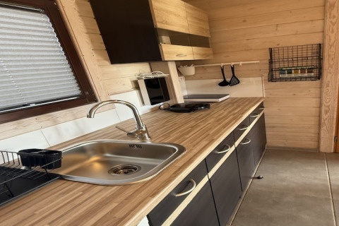 Moderne keuken in houten chalet met spoelbak, kookplaat, hangende tools en wandrekje met kruiden.
