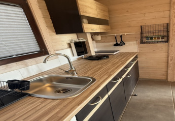 Cucina moderna in legno di un cottage con lavello, fornello, utensili appesi e porta spezie a muro.