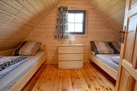 Soveværelse i en træhytte med to enkeltsenge, kommode og vindue hos Two-storey holiday cottages i Mielenko