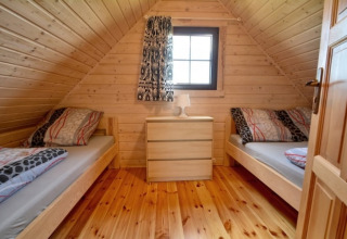 Slaapkamer met twee eenpersoonsbedden, een ladekast en raam in een houten lodge bij Mielenko, Denemarken