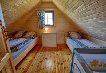 Zimmer mit Holzvertäfelung, zwei Einzelbetten, Kommode und Kinderbett im Ferienhaus in Mielenko.