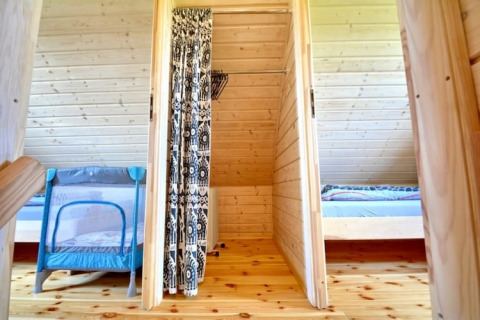 Binnenzicht van een houten lodge met schuine plafonds, twee slaapkamers en een kinderbedje in Mielenko.