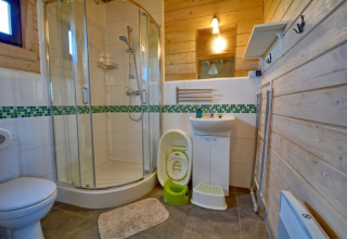 Moderne badeværelse i træhytte med brusekabine, håndvask, spejl, toilet og børneudstyr i Mielenko.