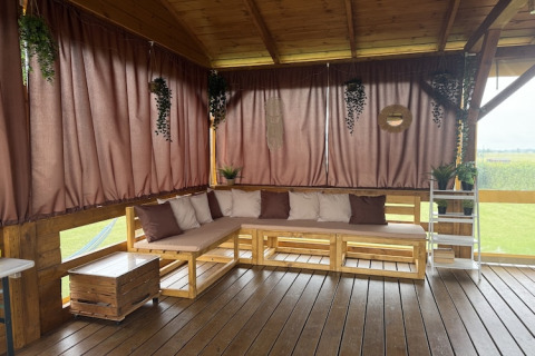 Udendørs terrasse med træsofa, puder og gardiner i brune nuancer ved lodge i Mielenko i Danmark.