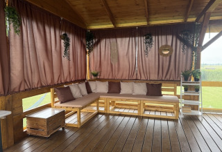 Udendørs terrasse med træsofa, puder og gardiner i brune nuancer ved lodge i Mielenko i Danmark.