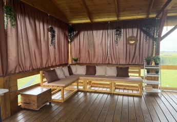 Houten terras met hoekbank, kussens en bruine gordijnen bij lodge Mielenko in Denemarken.