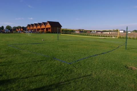 Grasveld met volleybalterrein en tweelaagse vakantiehuisjes bij Mielenko-lodge op een zonnige dag.