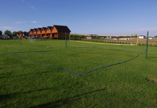 Grasveld met volleybalterrein en tweelaagse vakantiehuisjes bij Mielenko-lodge op een zonnige dag.