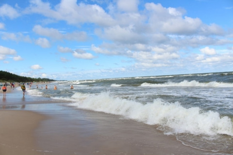 Strandbillede tæt på Mielenko, Danmark, med bølger, badende gæster og blå himmel med skyer.