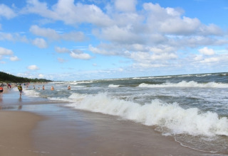 Strandbillede tæt på Mielenko, Danmark, med bølger, badende gæster og blå himmel med skyer.