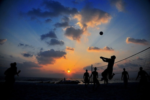 Mensen spelen beachvolleybal bij zonsondergang aan de kust bij Two-storey holiday cottages, Mielenko, Denemarken.