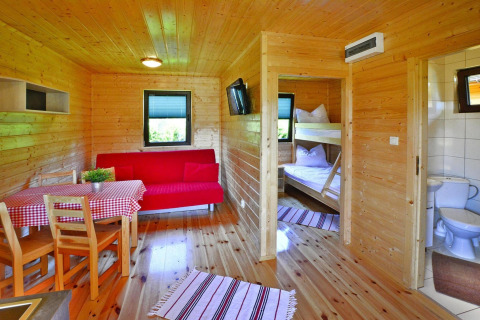 Binnenzijde van houten zomerhuis met eettafel, rode bank, stapelbed en badkamer, Mielno, Denemarken.