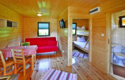 Innenansicht einer Holzhütte mit Essbereich, rotem Sofa, Etagenbett und Bad, Mielno, Dänemark.